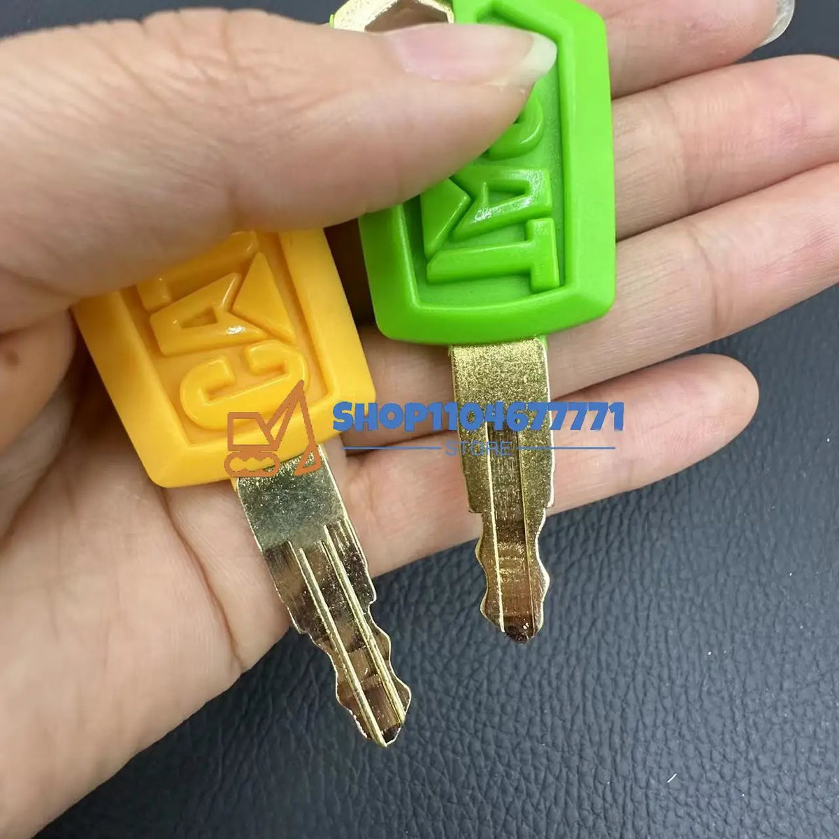A hand holds a set of replacement ignition keys for Caterpillar excavators, featuring green and yellow plastic components.
