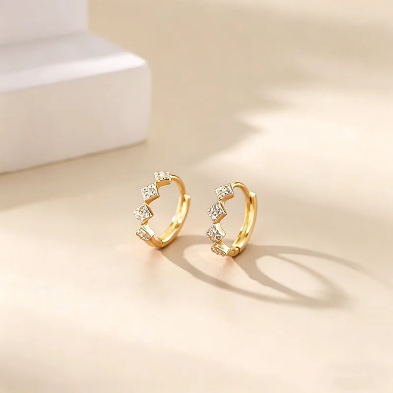 Pendientes de aro dorados adornados con pequeñas piedras de circonita de cúbica sobre una superficie clara.