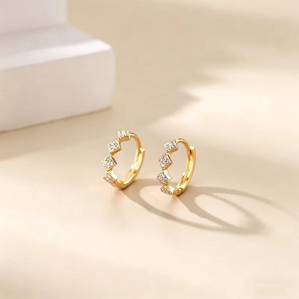 Gold hoop earrings adorned with small cubic zirconia stones resting on a light surface.