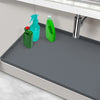 A flexible silicone under-sink mat with a raised edge is shown in a kitchen context with various cleaning bottles.