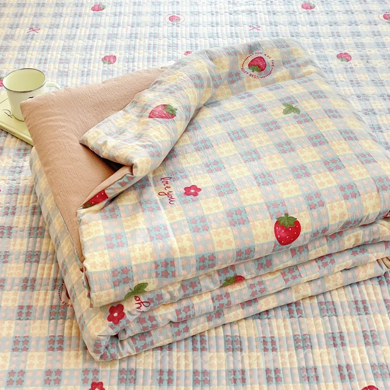A stack of cartoon pattern kids lightweight summer quilts in pale yellow and pink checkered fabric.