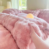 A hand is touching a fluffy pink fleece duvet cover with a rabbit design on a bed.