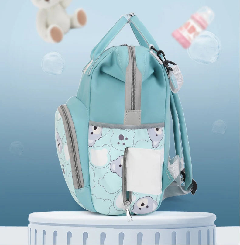 A light blue backpack with a bear print design and a white pocket is shown against a soft blue background.