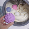 A hand holds a purple laundry ball inside a laundry pod with other colored balls and fabric.