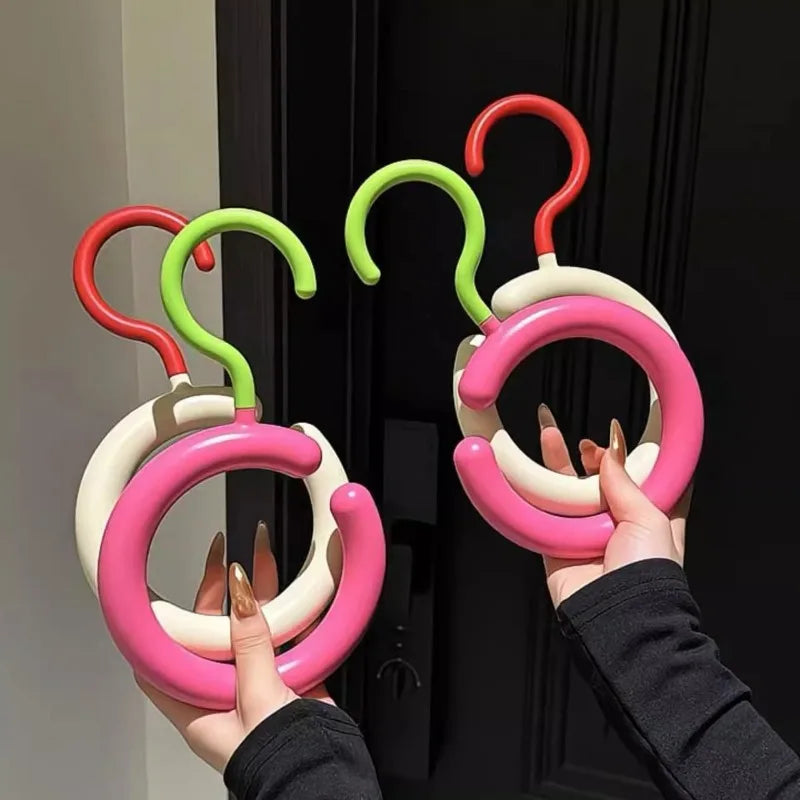 A hand is holding a pink Nordic wall-mounted hat and scarf organizer hook with green and red colored loops.