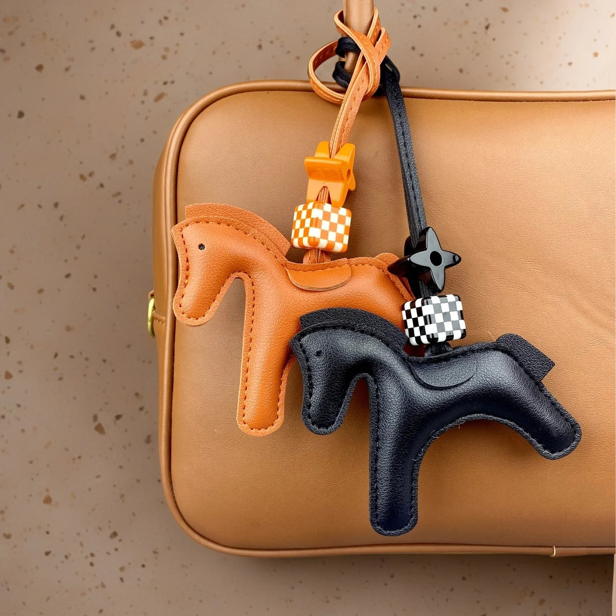 A leather pony charm in orange and black is attached to a tan leather handbag.