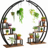 A black metal half moon plant stand with five tiers and hanging hooks displaying various green plants.