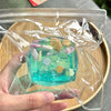 A hand holds a clear plastic bag containing a turquoise ocean-themed squeeze toy with seashells and sea life.