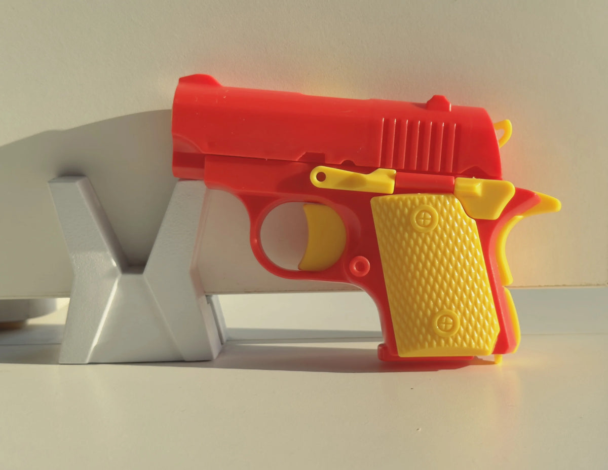A small, red and yellow 3D printed gravity fidget pistol toy resting on a white surface.