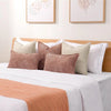 A collection of soft chenille throw pillow covers in beige, pink, and taupe on a white bed.