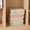 Stack of clear mesh storage bags filled with pink and white bedding inside a wooden cabinet