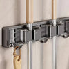 A wall-mounted metal holder for a mop and broom with detachable hooks, featuring silver and beige components.