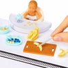 A mini doll kit featuring a baby figure and various miniature food accessories like bananas and other fruits.