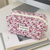 A floral quilted makeup bag with a zipper closure featuring red and pink roses on a white background.