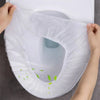 A hand is placing a white waterproof disposable toilet seat cover mat onto a toilet bowl.