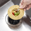 A hand is pouring water through a yellow silicone sink drain filter strainer into a metal sink.