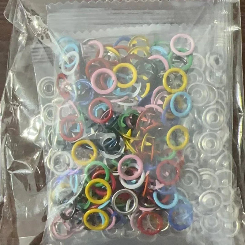 Bolsa de plástico transparente llena de anillos y hebillas metálicas de varios colores para ropa y bolsos