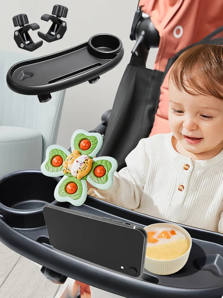 A child is using a black stroller snack tray with a cup holder and phone slot, featuring a decorative food item.