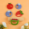 A set of silicone fruit-shaped baby teethers, including an apple and a strawberry, are displayed on a light orange background