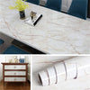 Rolls of pearlescent pink marble peel and stick wallpaper displayed on a white marble surface.