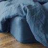 A close-up of a wrinkled, deep blue linen fitted sheet draped over a dark blue pillow.