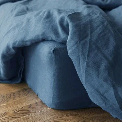 A close-up of a wrinkled, deep blue linen fitted sheet draped over a dark blue pillow.