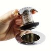A hand holds a stainless steel bathtub drain with a mesh hair catcher over a metal plate.