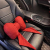 A red butterfly bow tie neck pillow with a matching fabric cover resting on a black car seat.