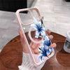 A hand holds a pink magnetic phone case featuring blue lily floral designs on a wooden surface.
