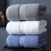 A stack of three folded bath towels in gray, white, and light blue on a black surface.