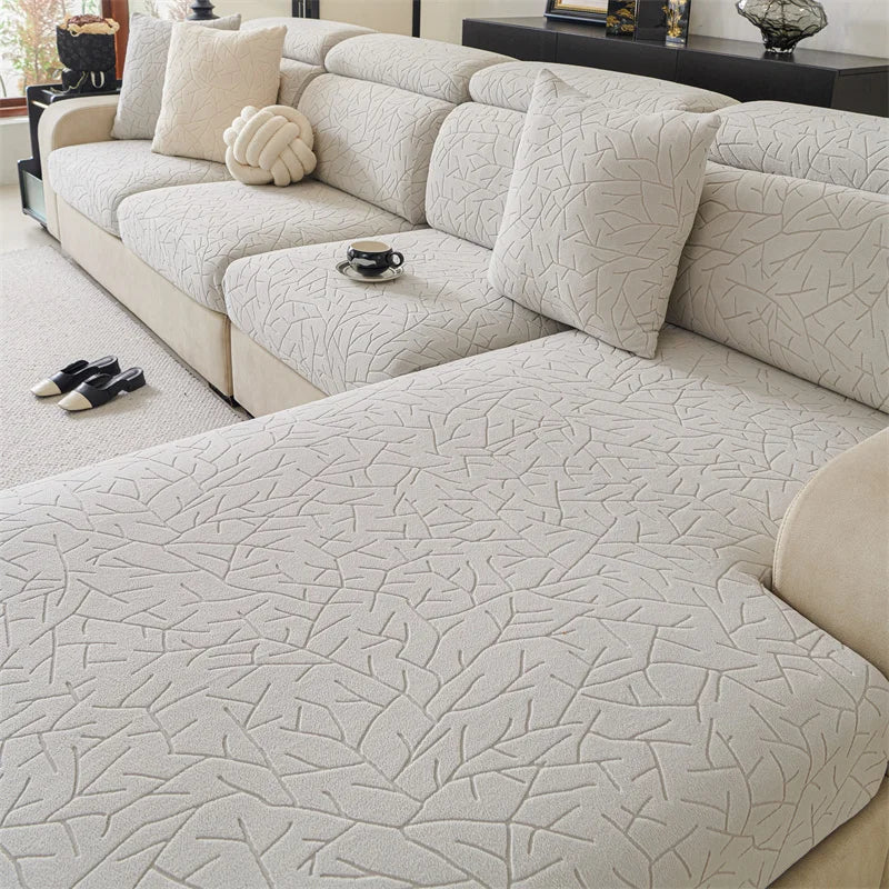 A light beige jacquard fleece sofa cover with a textured pattern and anti-slip backing shown on a sectional sofa.