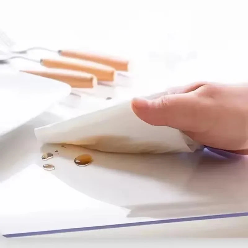 A hand is placing a white sheet of clear PVC waterproof table protector onto a white surface.