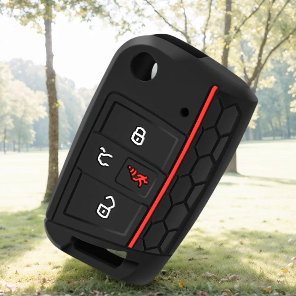 A black silicone car key fob cover with red accents resting on green grass.