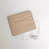 A beige genuine leather slim card holder wallet in a clear plastic sleeve.