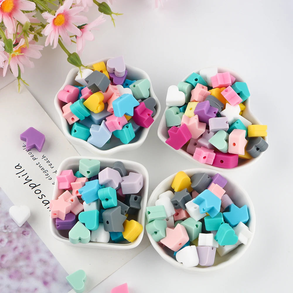 A collection of colorful silicone crown star heart beads in various shades are displayed in small white bowls on a white back