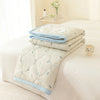 A light blue quilted summer quilt with small butterfly embroidery is folded on a white bed.