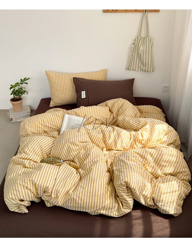 A beige and gold striped duvet cover set displayed on a brown bed with pillows and a potted plant.
