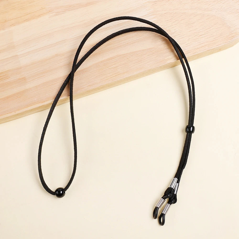 Black adjustable soft eyewear lanyard with a metal clip resting on a light wooden surface.