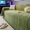 A green fishbone pattern anti-slip sofa cover draped over a sofa with a cream pillow and a white cup.