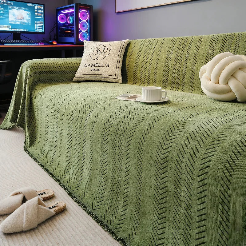A green fishbone pattern anti-slip sofa cover draped over a sofa with a cream pillow and a white cup.