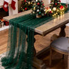 A dark green pearl beaded tulle table runner draped over a wooden table in an indoor setting.