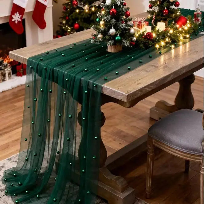 A dark green pearl beaded tulle table runner draped over a wooden table in an indoor setting.