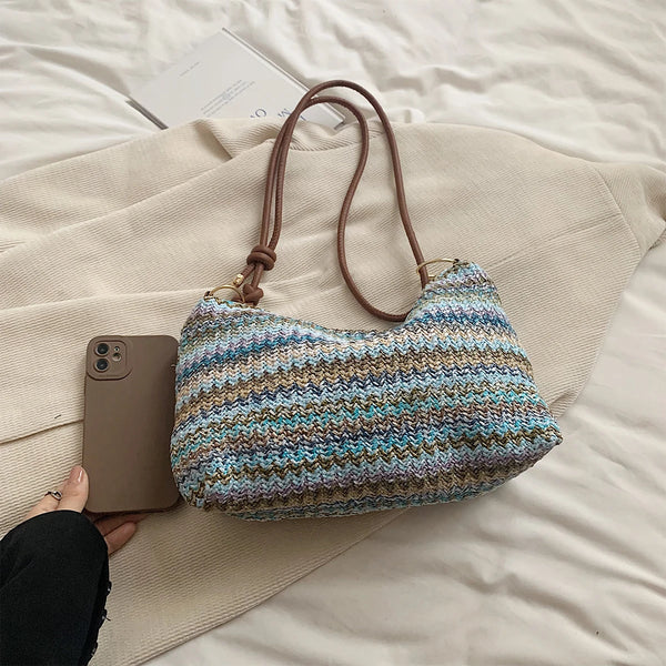 A woven straw tote bag with multicolored stripes rests on a light beige blanket next to a smartphone.