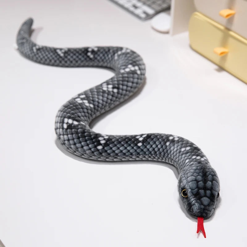 A gray and black patterned lifelike snake plush toy is coiled on a white surface.