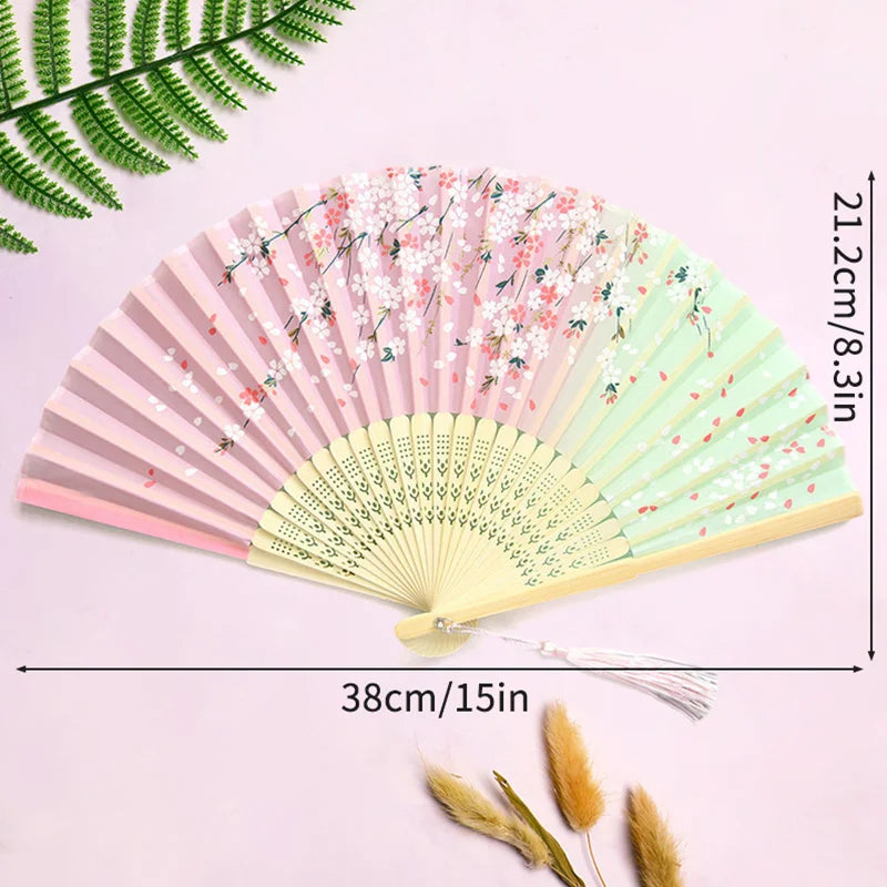 A pink and green vintage lace folding hand fan with a durable handle displayed on a light purple background.