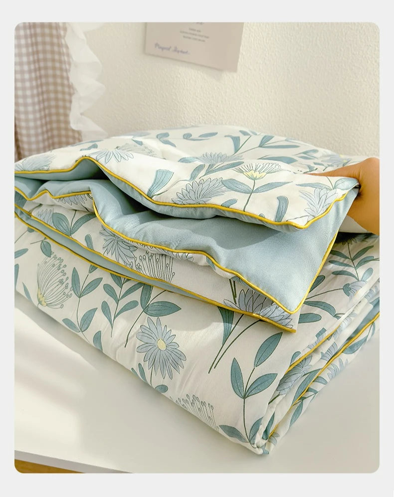 A light blue and white floral patterned quilt folded on a white surface.