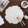 Weiß vergoldete Pfingstrosen-Platzsets mit feinen floralen Mustern auf einem dunkelbraunen Tisch.