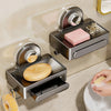 Chrome wall-mounted soap dish with drain tray holding pink soap and a yellow bar of soap