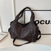 A dark brown vintage leather tote bag with a shoulder strap is displayed on a white surface.
