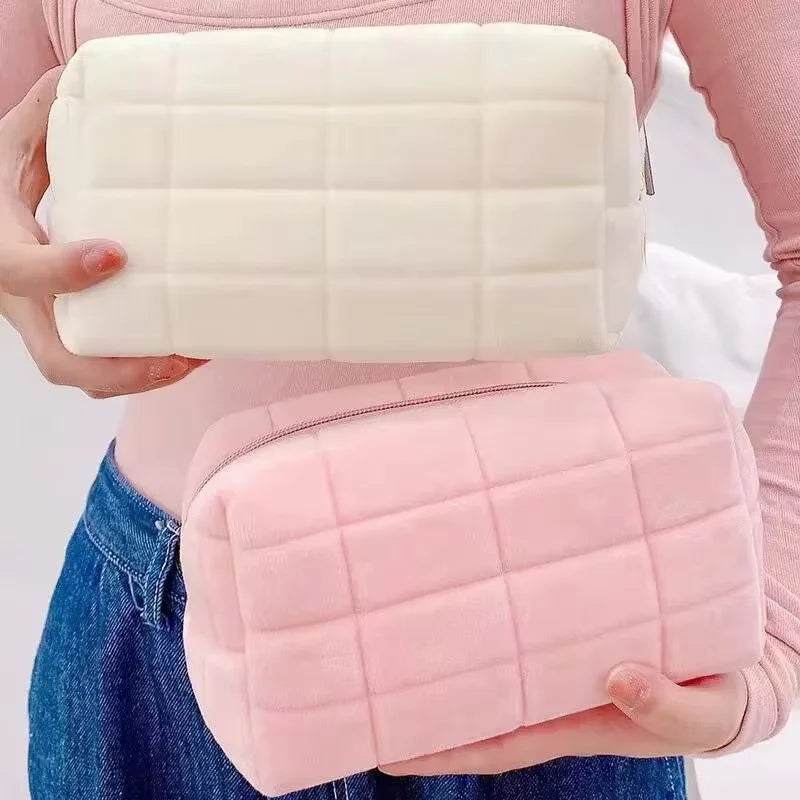 A person holds two quilted makeup bags, one white and one pink, against a light background.